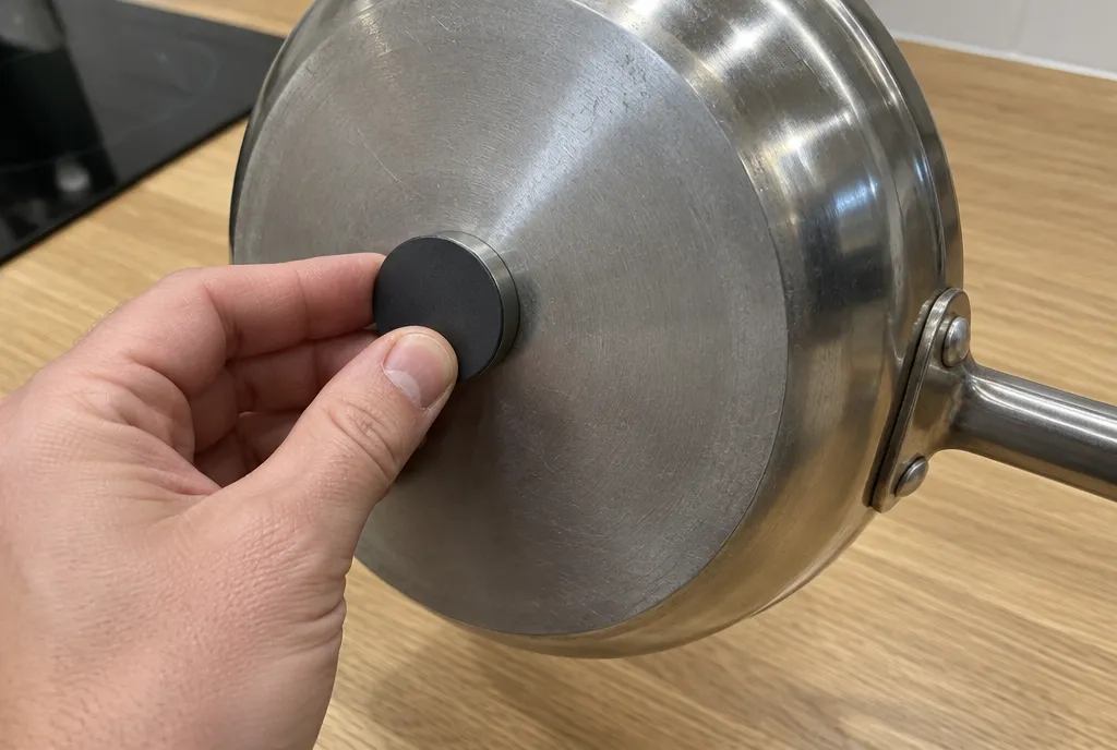 A round fridge magnet stuck to the underside of a stainless steel pan
