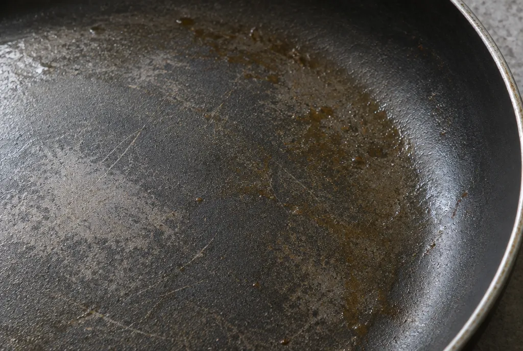 Close-up of a worn non-stick coating with scratches and a sticky residue from cooking spray